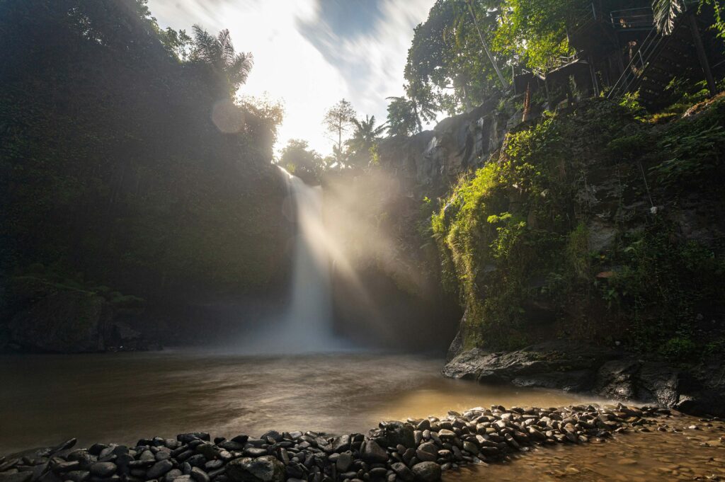 Tegenungan Waterfall glowing under golden sunset light with tropical mist